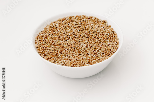 Bowl of uncooked buckwheat grains on white isolated background