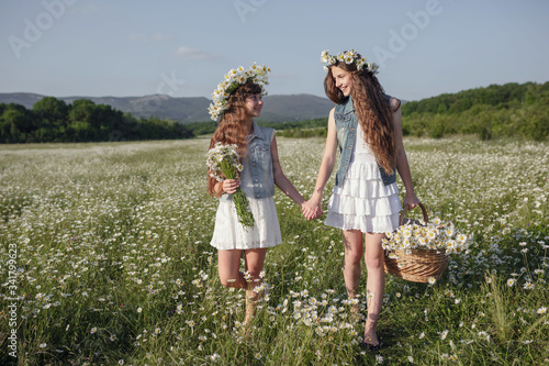 two cute teen girls in denim overalls walk in a daisy field