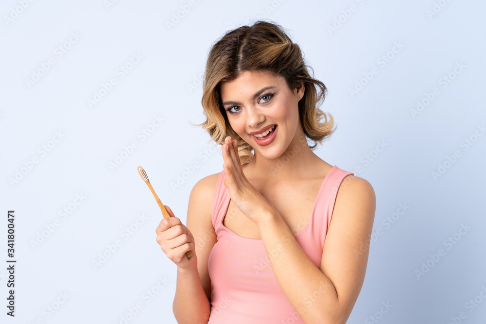 Teenager girl brushing her teeth isolated on blue background whispering something Teenager girl brushing her teeth isolated on blue background whispering something