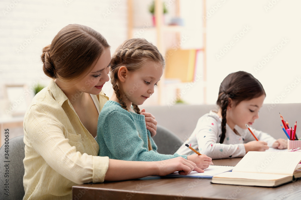 Mother helping her daughters with homework at table indoors Mother helping her daughters with homework at table indoors