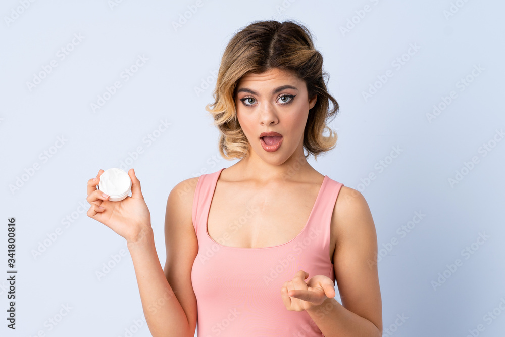 Young girl with moisturizer surprised and pointing front Young girl with moisturizer surprised and pointing front
