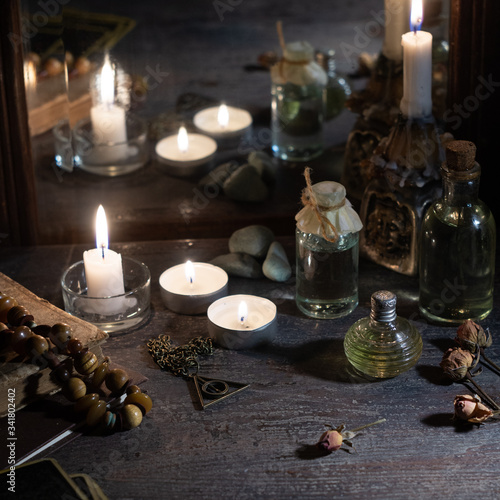Burning candles, fortune-telling cards and tincture bottles are reflected in an old mirror