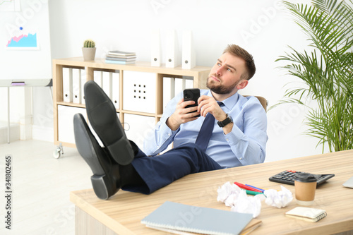 Lazy office employee with mobile phone at workplace