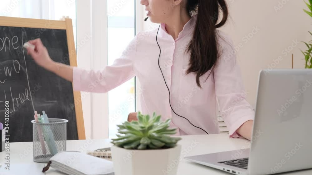 Young woman in headset speaking by webcam and using laptop. Video call and home schooling, teacher working from home Young woman in headset speaking by webcam and using laptop. Video call and home schooling, teacher working from home