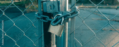 Locked Gate Tethered by metal chain and old rusty padlock on sunshines background. Wide photo.