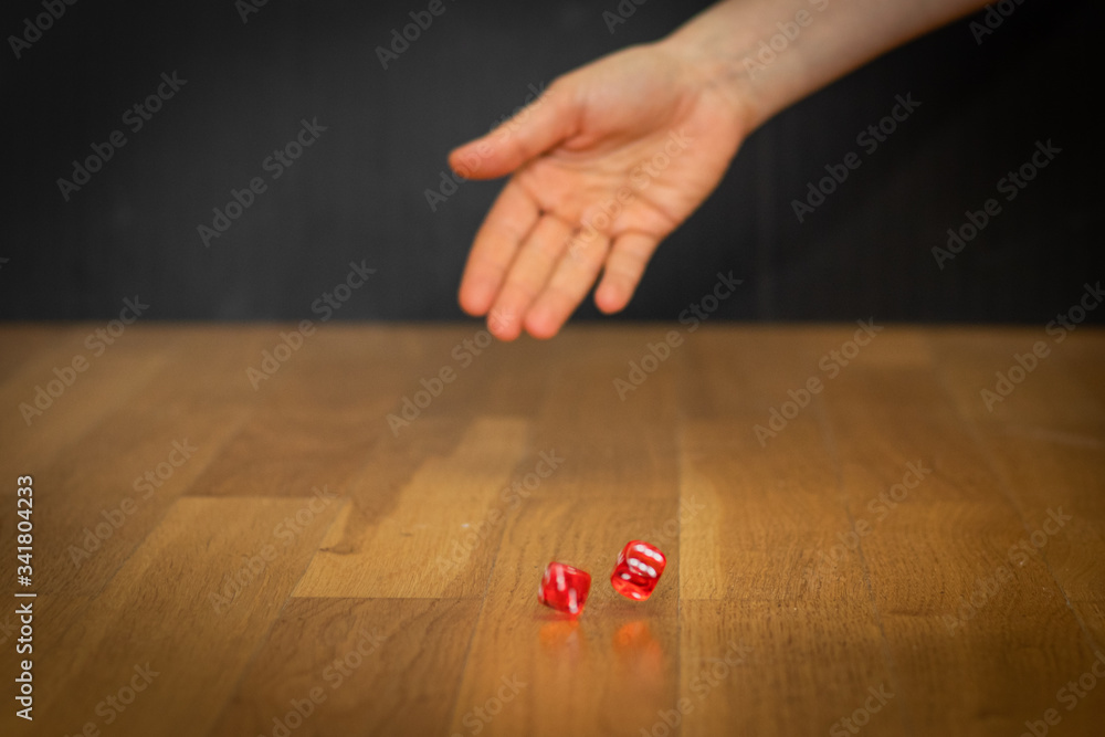 Obraz premium main jetant deux dés rouges sur le plancher de parquet avec le fond noir