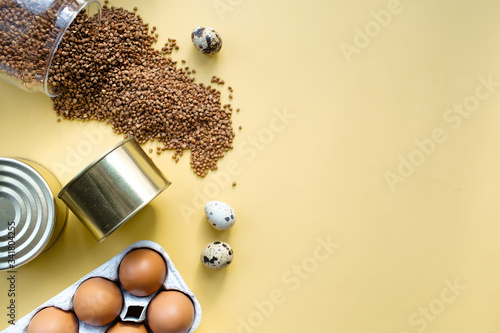 Food supplies crisis food stock for quarantine isolation period on yellow  background.
Buckwheat, eggs, canned food. Food delivery, Donation, coronavirus quarantine. Copyspace. photo