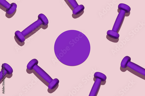 Sports pattern. Purple dumbbells scattered on a pink mat. The circle in the center of the frame for the text.