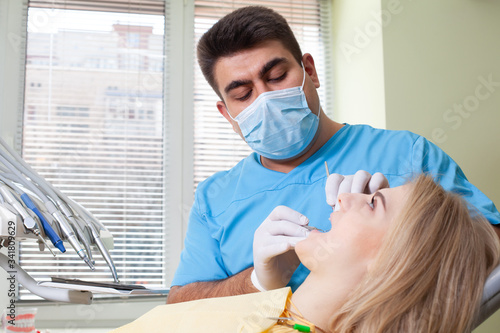 Dentist examining patient s teeth  wearing blue uniform and gloves  looking at patient s teeth carefully with dental instruments