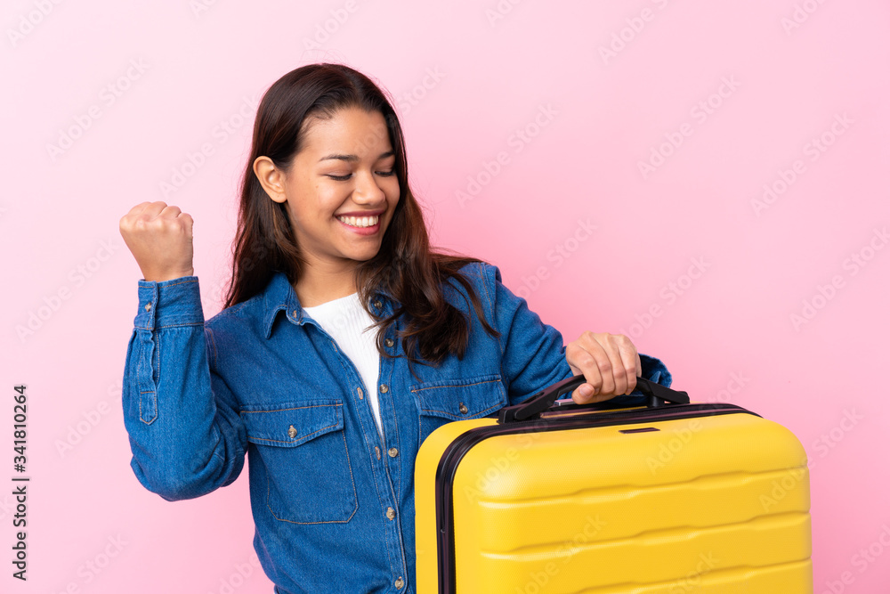 Traveler Colombian woman holding a suitcase over isolated pink background celebrating a victory Traveler Colombian woman holding a suitcase over isolated pink background celebrating a victory