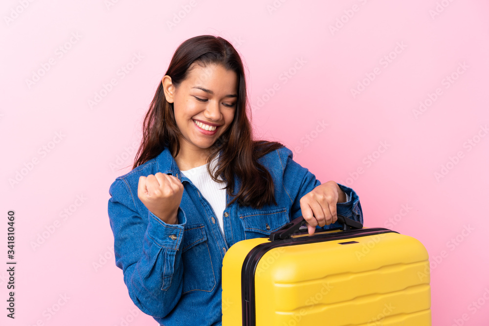 Traveler Colombian woman holding a suitcase over isolated pink background celebrating a victory Traveler Colombian woman holding a suitcase over isolated pink background celebrating a victory