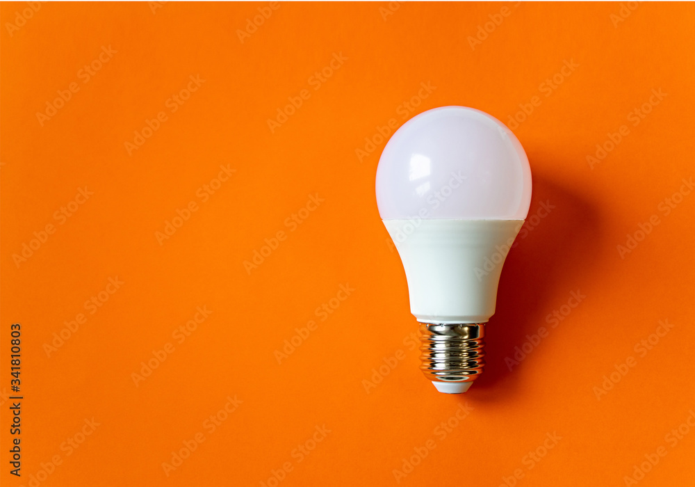 White energy saving light bulb on an orange background with copy space. LED white bulb, concept of new idea - obrazy, fototapety, plakaty 