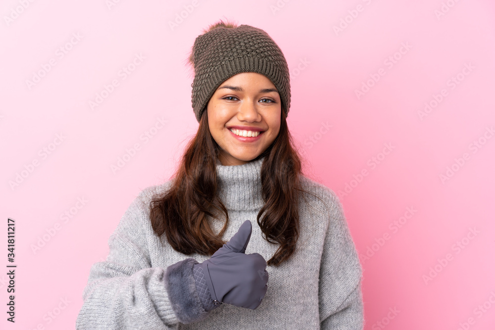 Young Colombian girl with winter hat over isolated pink wall giving a thumbs up gesture Young Colombian girl with winter hat over isolated pink wall giving a thumbs up gesture