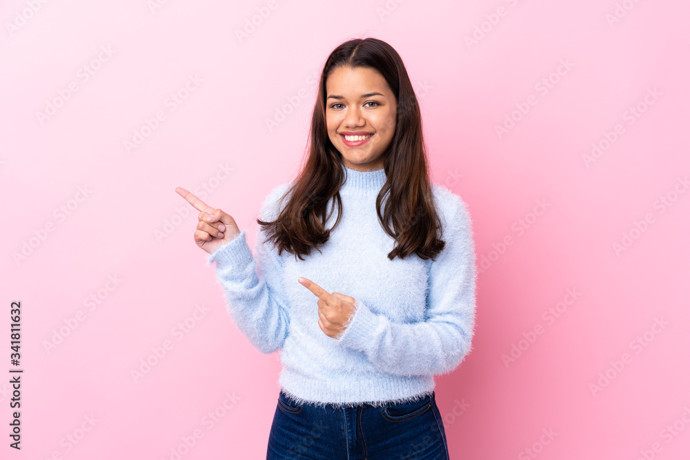 Young Colombian girl over isolated pink background pointing finger to the side Young Colombian girl over isolated pink background pointing finger to the side