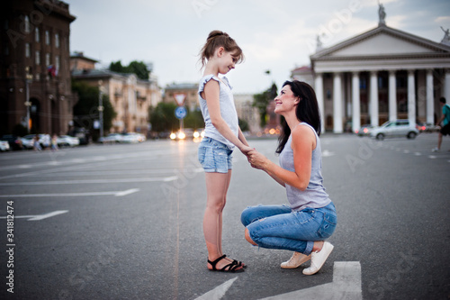 mother and daughter in jeans look at each other and smile against the background of the evening city