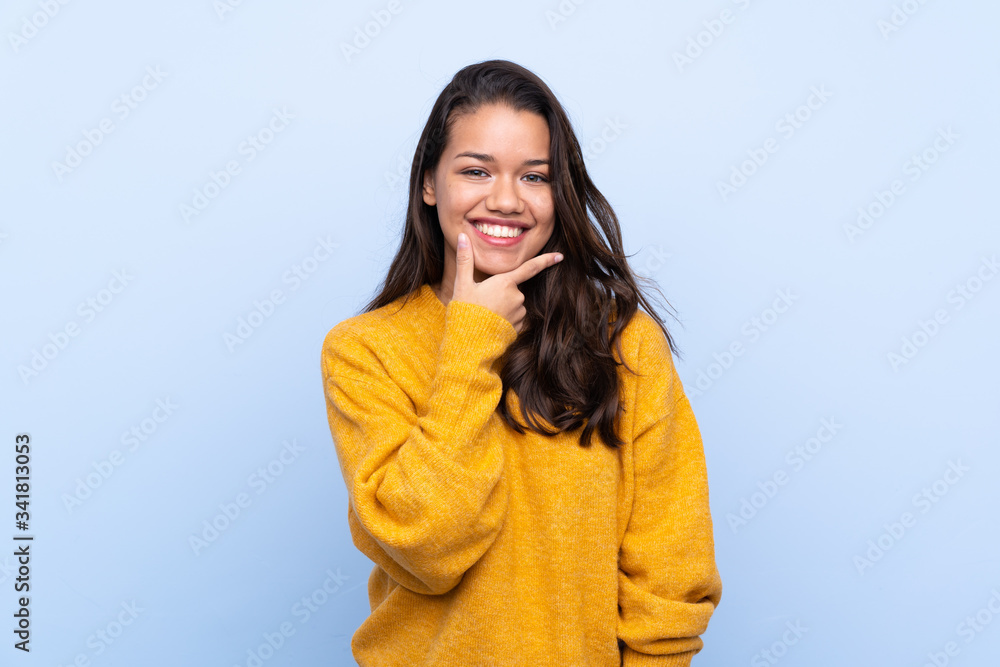 Young Colombian girl with sweater over isolated blue background smiling Young Colombian girl with sweater over isolated blue background smiling