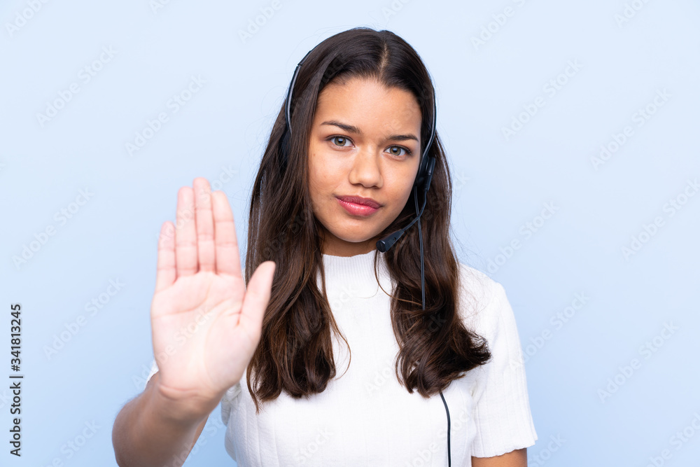 Young telemarketer Colombian woman over isolated blue background making stop gesture with her hand Young telemarketer Colombian woman over isolated blue background making stop gesture with her hand