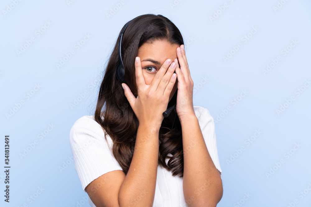 Young telemarketer Colombian woman over isolated blue background covering eyes and looking through fingers Young telemarketer Colombian woman over isolated blue background covering eyes and looking through fingers
