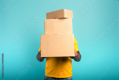 Man is hidden by too many received packages. Cyan background