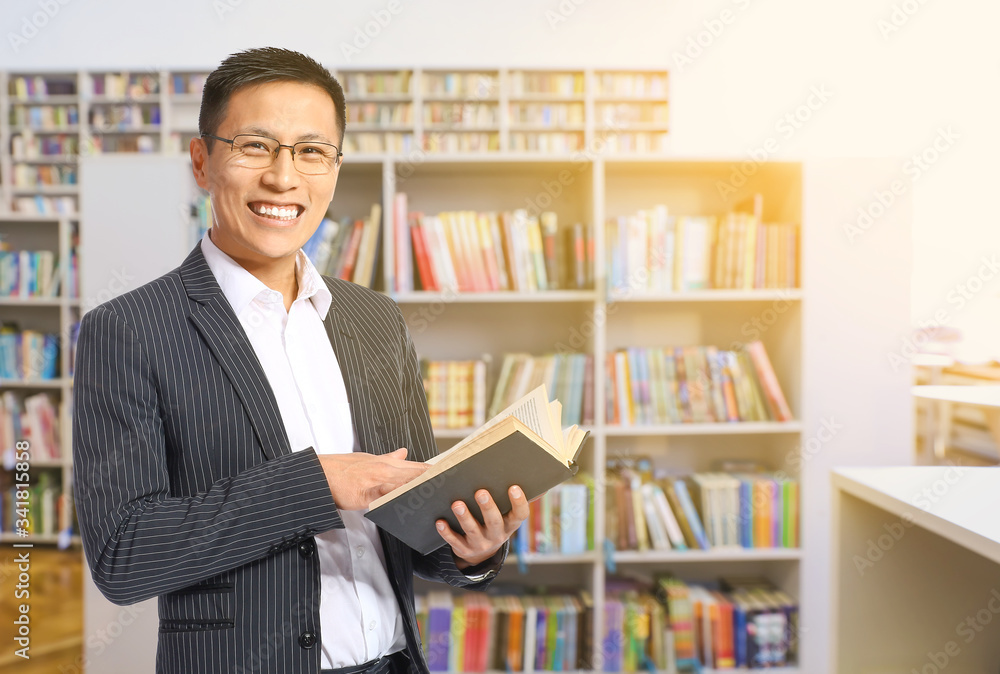 Handsome Asian man with book in modern library