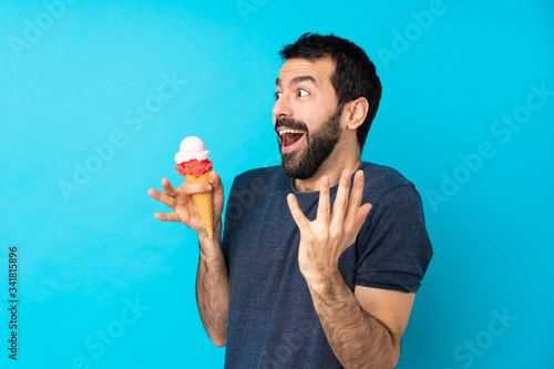 Young man with a cornet ice cream over isolated blue background with surprise facial expression