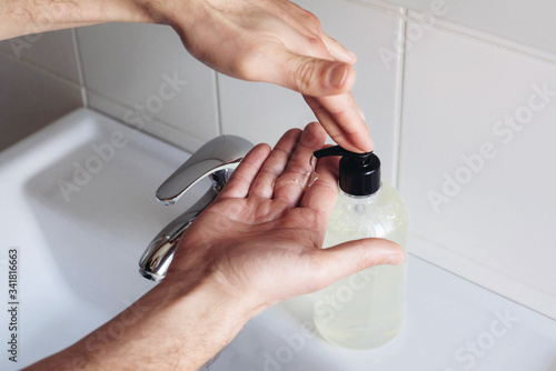 Man cleaning his hands using liquid disinfectant soap and water in bathroom.