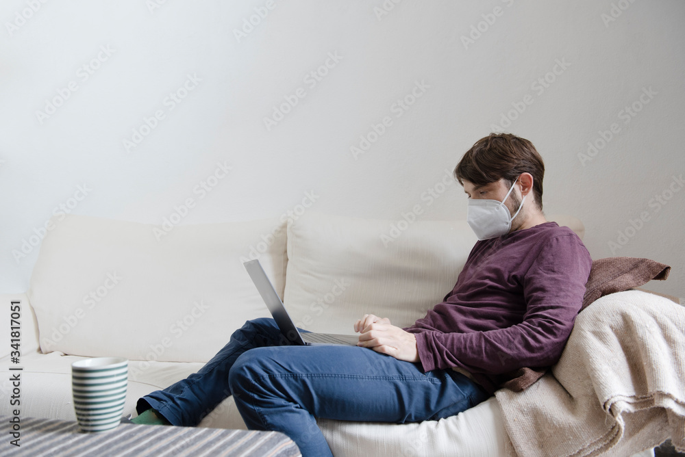 man working on his computer from the couch with a face mask