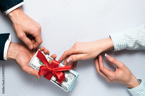 Concept, money as a gift, win or bonus. businessman takes or gives pile of 100 dollar bills tied with red ribbon with bow to woman. Flat lay top view copy space.