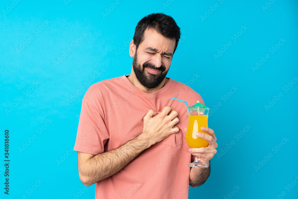 Young man over holding a cocktail over isolated blue background having a pain in the heart Young man over holding a cocktail over isolated blue background having a pain in the heart