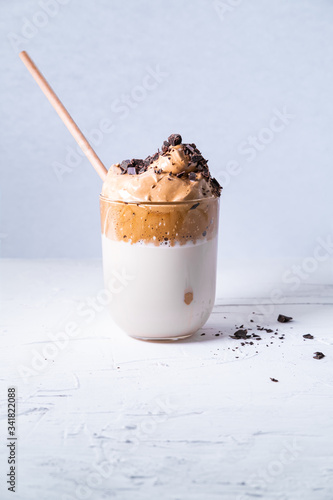 Dalgona coffee in a glass with chocolate chips and bamboo straw on white background. Vertical picture.