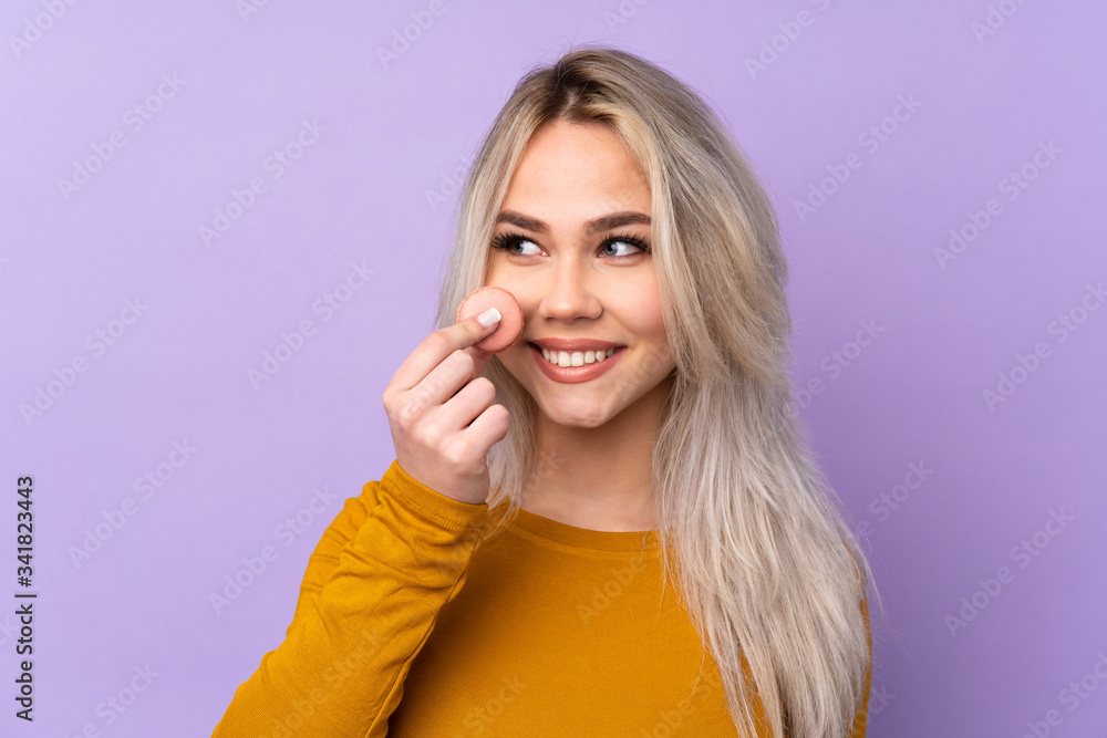 Teenager girl over isolated purple background holding colorful French macarons Teenager girl over isolated purple background holding colorful French macarons
