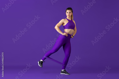 Strong. Beautiful young female athlete practicing in studio  monochrome purple portrait. Sportive caucasian fit model with elastics. Body building  healthy lifestyle  beauty and action concept.