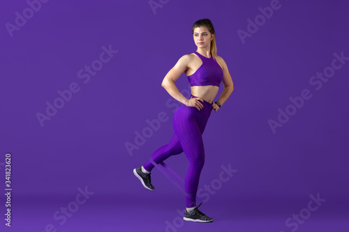 Strong. Beautiful young female athlete practicing in studio, monochrome purple portrait. Sportive caucasian fit model with elastics. Body building, healthy lifestyle, beauty and action concept.