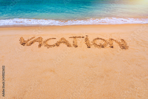 Vacation text on a beach. Vacation written in a sandy tropical beach. "Vacation" written in the sand on the beach blue waves in the background. Vacation on the sand beach concept.