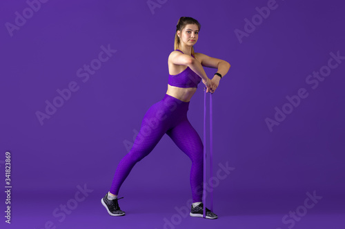 Strong. Beautiful young female athlete practicing in studio, monochrome purple portrait. Sportive caucasian fit model with elastics. Body building, healthy lifestyle, beauty and action concept.