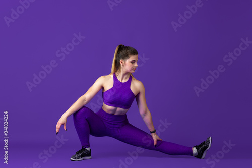 Stretching. Beautiful young female athlete practicing in studio, monochrome purple portrait. Sportive caucasian fit model training. Body building, healthy lifestyle, beauty and action concept.