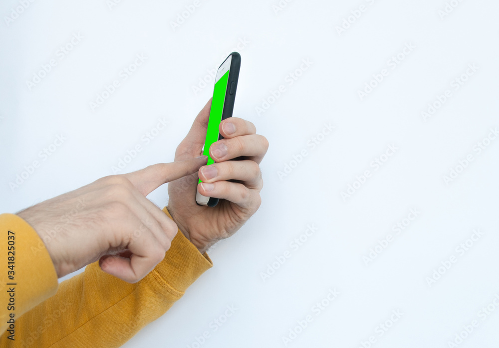 Male hands in a yellow sweater holding and tapping or working with smartphone isolated on white background. Smartphone with green screen Male hands in a yellow sweater holding and tapping or working with smartphone isolated on white background. Smartphone with green screen