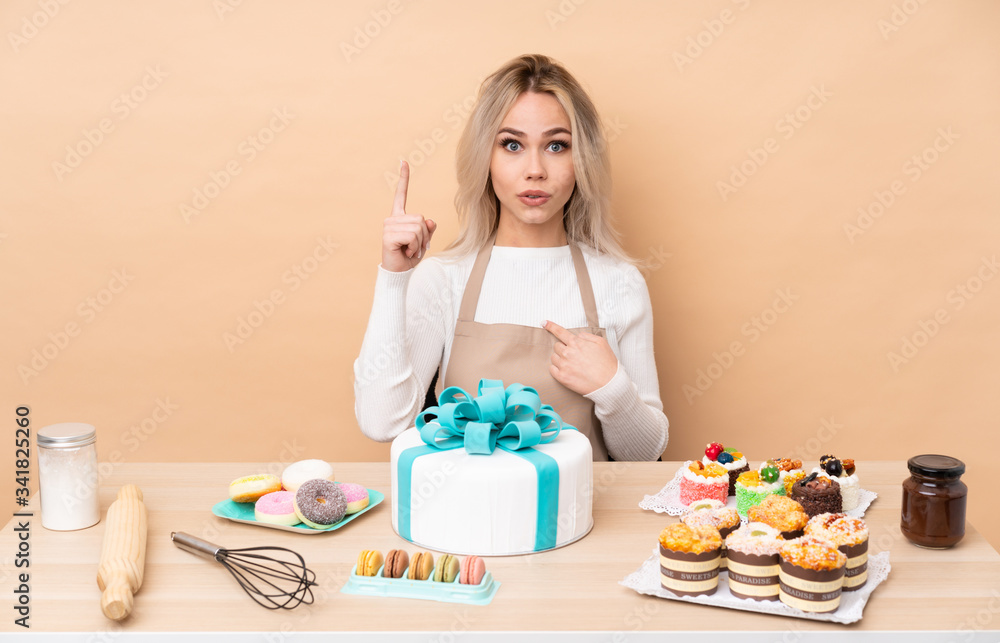 Teenager pastry chef with a big cake in a table with surprise facial expression Teenager pastry chef with a big cake in a table with surprise facial expression