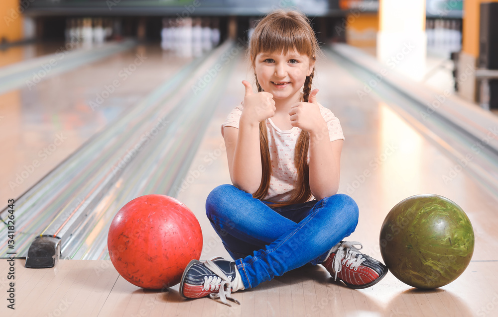 Fototapeta premium Little girl playing bowling in club