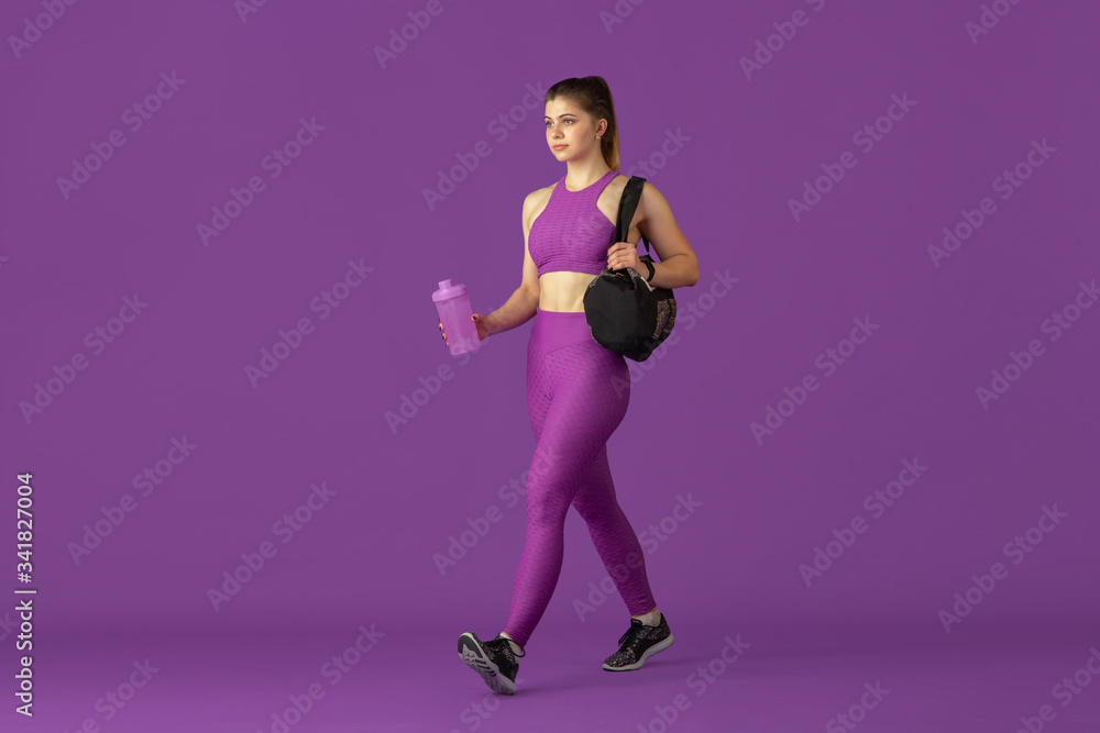 Beautiful young female athlete practicing in studio, monochrome purple portrait. Sportive caucasian fit model going to training with bag. Body building, healthy lifestyle, beauty and action concept.