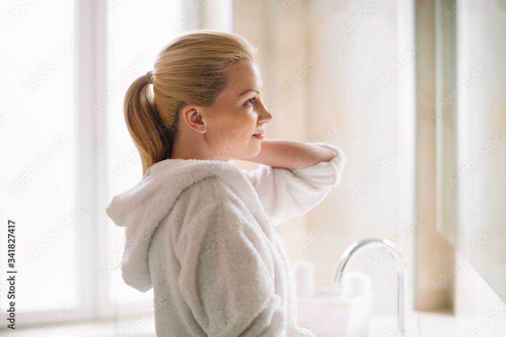 Young woman in bathrobe use the cream for the body. Beautiful woman enjoying in hotel. Young woman in bathrobe use the cream for the body. Beautiful woman enjoying in hotel.