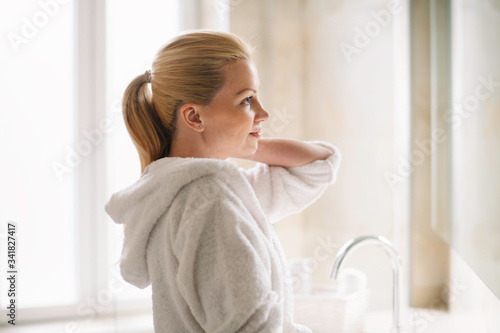 Young woman in bathrobe use the cream for the body. Beautiful woman enjoying in hotel.