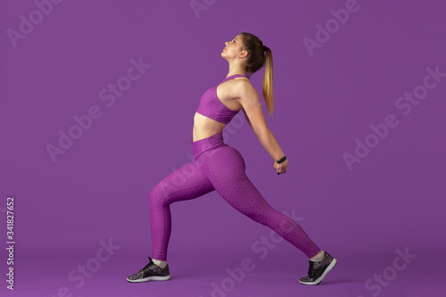Stretching. Beautiful young female athlete practicing in studio, monochrome purple portrait. Sportive caucasian fit model training. Body building, healthy lifestyle, beauty and action concept.