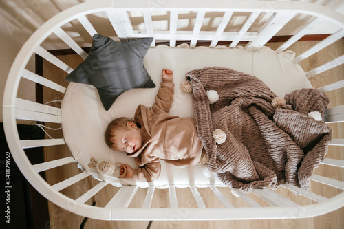 Cute little 1-year-old baby is lying on a cot while sleeping with Windows of light on his face