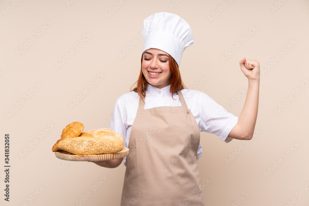 Redhead teenager girl in chef uniform. Female baker holding a table with several breads celebrating a victory Redhead teenager girl in chef uniform. Female baker holding a table with several breads celebrating a victory