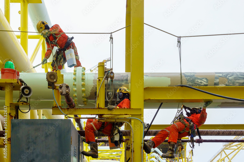 Working at height. A group of abseilers wearing red coverall and Personal Protective Equipment