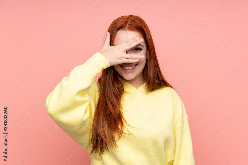 Redhead teenager girl over isolated pink background covering eyes by hands and smiling