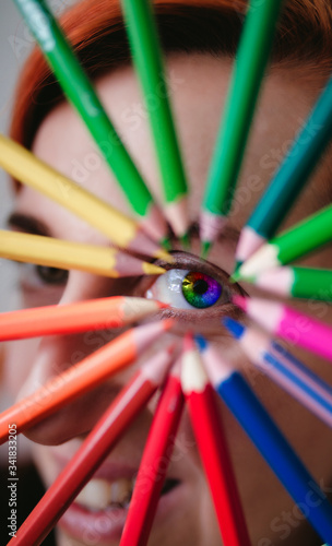 Portrait of a beautiful young woman with a colorful eye in the rainbow. Highlighted by a circle made of pencils as a symbol of art,education and inspiration.