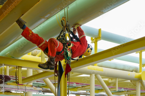 Working at height. An abseiler wearing Personal Protective Equipment (PPE) climbing under of oil and gas platform for touch up painting on pipeline. photo