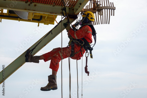Working at heightWorking at height. A group of abseilers wearing red coverall and Personal Protective Equipment (PPE) hanging under access way platform to check the corrosion of the structure.
